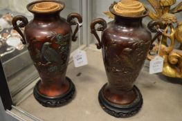 A pair of Japanese decorative bronze twin handled vases with hardwood stands.