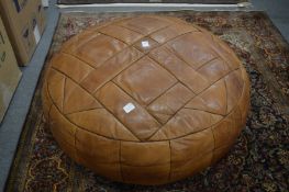 A large brown leather upholstered pouffe.