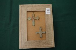 Two bronze crucifixes on a framed mount.