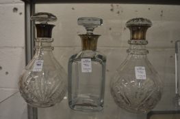 A pair of silver top cut glass decanters and another silver top decanter.