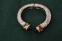 A silver torque style bangle set with green and red stones.