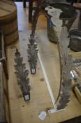 A pair of leaf shaped metal curtain tie-backs and a metal leaf shaped bracket or side table frame.