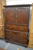 A George III oak housekeepers cupboard with a pair of panelled doors above a secretaire drawer