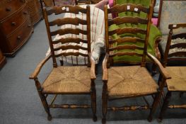 A pair of rush seated ash ladderback dining chairs with arms.