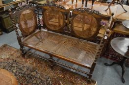 A 17th century style oak settee with cane work back panels and seat with barley twist supports.