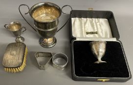 Cased silver egg cup, 2 small silver trophies, 2 silver napkin rings & a silver backed hair brush.