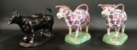 Two pink lustre cow creamers on domed grassy base, oval covers, 19cm wide and a black glazed