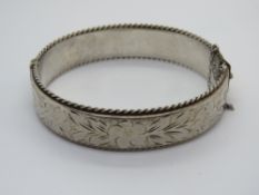 A hallmarked silver hinged bangle having floral engraving throughout.