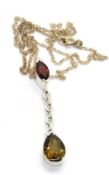 A silver pendant having pear cut stone suspended below red marquise cut stone,