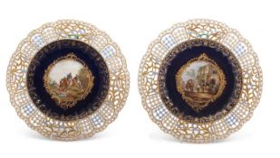 A pair of 19th Century Meissen plates, the centre painted with landscape designs with figures, the