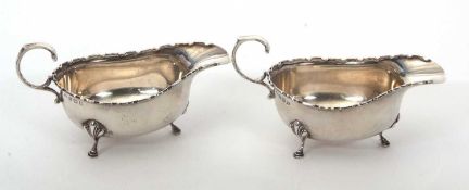 A pair of George V silver sauce boats of typical form with applied castellated rims, flying scroll