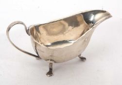 A George VI silver sauce boat of typical form having a wavy rim and c scroll handle, supported on