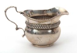 An Edwardian silver small cream jug of oval plain form, the top section of the body decorated with a