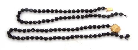 A black bead necklace with gold clasp, the cushion shape clasp with raised letter T design