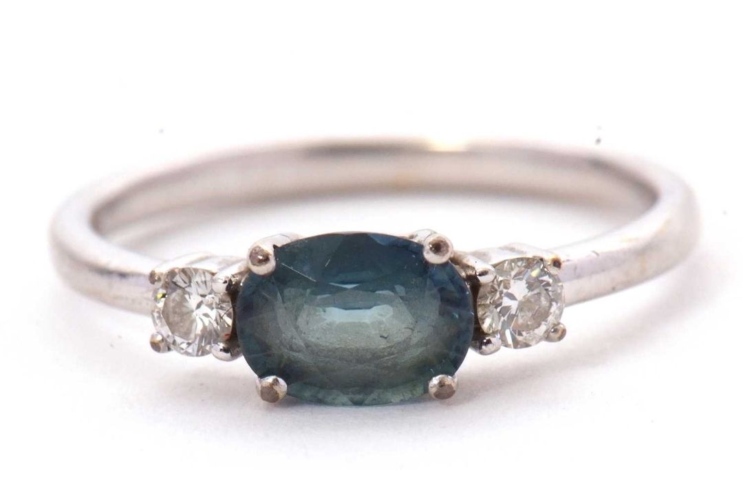 A 9ct sapphire and diamond ring, the oval blue-green sapphire set to either side with a round - Image 1 of 8