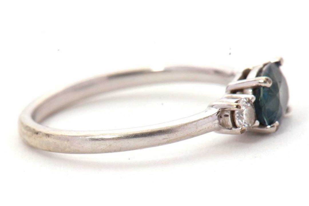 A 9ct sapphire and diamond ring, the oval blue-green sapphire set to either side with a round - Image 2 of 8