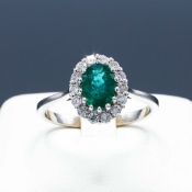 AN 18CT WHITE GOLD EMERALD AND DIAMOND CLUSTER RING.