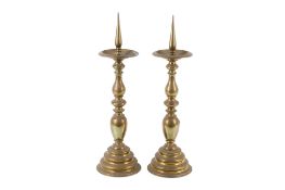 A pair of brass candlesticks. Having flared tops with baluster columns raised on stepped bases.