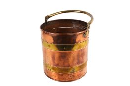 A vintage copper bucket with brass strapping and a swing handle.