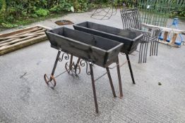 A pair of trolley trough style planters. Wood on metal bases, with two wheels each to one side and a