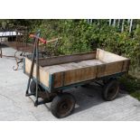 A metal and wooden four-wheeled trolley or trailer. With two axles; the front attached to handles