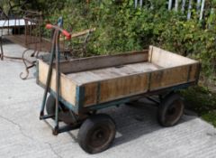 A metal and wooden four-wheeled trolley or trailer. With two axles; the front attached to handles