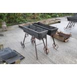 A pair of trolley trough style planters. Wood on metal bases, with two wheels each to one side and a