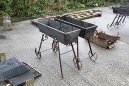 A pair of trolley trough style planters. Wood on metal bases, with two wheels each to one side and a