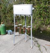 A vintage metal four-bottle filling machine. With an open tank raised on three legs, four valves