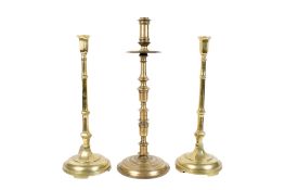 Three large brass candlesticks. Consisting of a pair and one other, all raised on circular bases.