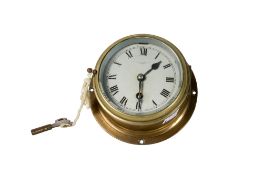 Small brass cased bulkhead ship's wall clock. Having a 10cm dial, key present.