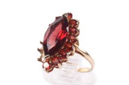 A 9ct gold garnet cluster ring. The large central marquise cut garnet circa 1.3cm x 0.