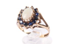 A 9ct gold and opal cluster ring. The central stone circa 7mm x 5mm, surrounded by small sapphires.