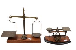 Two sets of vintage brass postage letter scales. Both with weights and raised on wooden plinths.