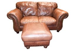 A modern brown leather two seater sofa and matching foot stool.