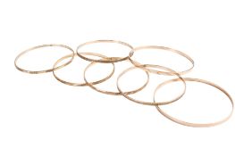 Seven 9ct gold (tested) narrow flat bangles of various designs, some marked. Gross weight 49.8g.