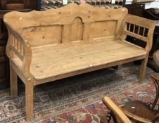 A pine bench with panelled back and galleried arms over a two plank seat on square legs 179 cm wide