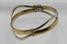 A 9ct two tone gold 'twisted' hinged snap bangle, approx 16.3g.