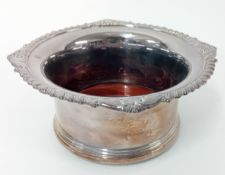 An ornate modern silver wine coaster, 'King's' shell pattern motif to rim, on a wooden base,