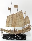 A Chinese silver model of a Chinese War Junk with three spread sails and figures on carved wood