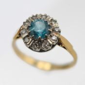 An 18ct cluster ring set with a central light blue topaz and small round cut diamond border, size P,