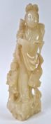 A soapstone figure of a lady, carved standing on a rock, wearing a long flowing robe with an acolyte