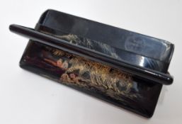 A lacquered cigarette case with gilt details, unfolding into an x-frame stand.