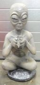 A large fiberglass/plastic figure of an Alien sitting and holding a large crystal