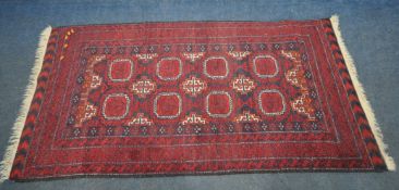 A RED GROUND RECTANGULAR RUG, with eight medallions, repeating geometric patterns, surrounded by a