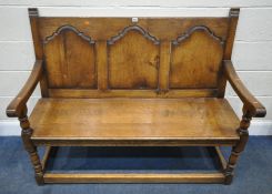 A REPRODUCTION GEORGIAN STYLE OAK SETTLE, with three fielded panels, open armrests, raised on turned