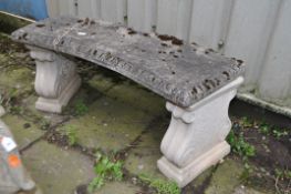 A WEATHERED COMPOSITE CURVED GARDEN BENCH, on twin scrolled supports, length 110cm x depth 40cm x