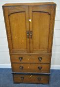 AN ARTS AND CRAFTS OAK GENTLEMAN'S WARDROBE, with a sloped cornice, the double doors enclosing three
