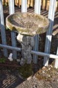 A WEATHERED COMPOSITE BIRD BATH, in the form of a cherub holding a bowl aloft, 42cm diameter, height