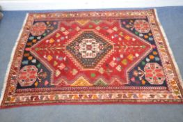 A RED GROUND RECTANGULAR WOOLEN RUG, with repeating geometric patterns, surrounded by a multi-